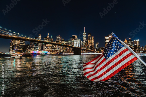 Brooklyn Bridge span above night harbor. City lights reflecting across river beneath suspension landmark