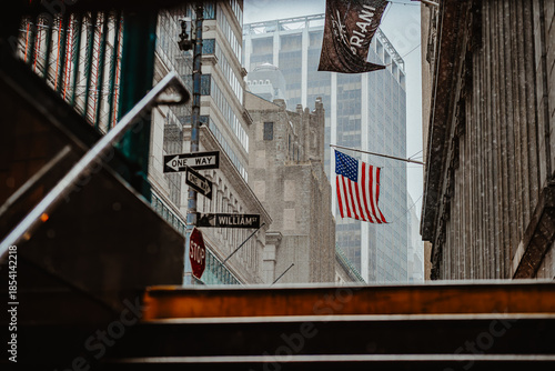 New York, USA, 9 December 2025: Stair exit revealing rainy downtown scene. City architecture and American flag visible from subway exit