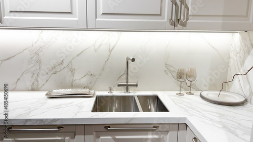 Slika na platnu Stylish modern kitchen interior with white marble countertop, double sink, sleek cabinets, under lighting