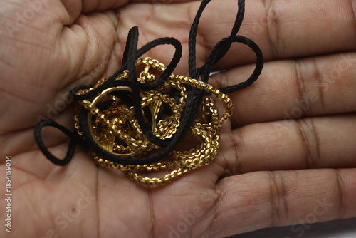 Holding a folded golden chain and golden ring along with a black thread. Real gold ornaments