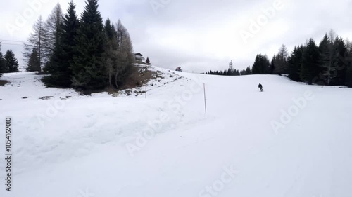 Skier Skiing Down a Groomed Piste in a Mountain Resort, Winter Vacation and Recreation Concept, Chairlift and Pine Trees in Background, Overcast Weather