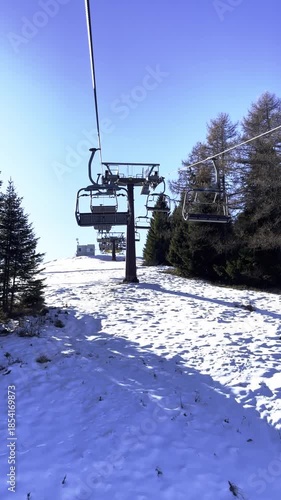 Chairlift Cable Car Moving Up Snowy Mountain Slope, Sunny Winter Day with Blue Sky, Ski Resort Transportation, Alpine Holiday Scenic View, Empty Chairs Passing By, Pine Trees, Vertical Video
