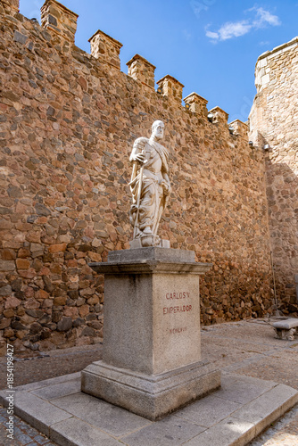 A white marble statue of Emperor Charles V stands on a granite pedestal inside the Puerta de Bisagra courtyard in Toledo, backed by ancient stone defensive walls