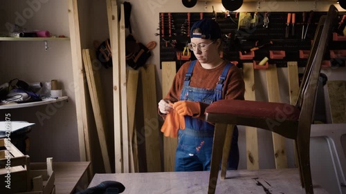 Female furniture restorer putting on orange protective gloves before working in renovation workshop
