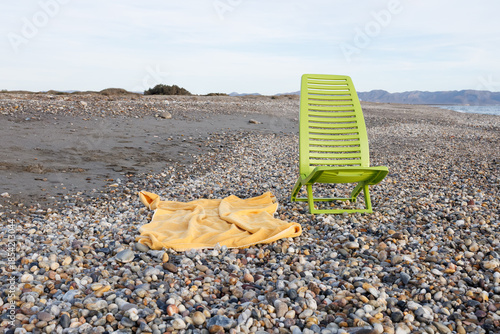 Empty pebble beach with vibrant green chair and towel