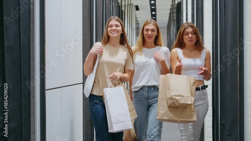 Three women smiling and talking while walking with shopping bags through fashion store corridor, concept of leisure and retail experience