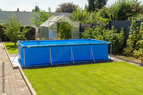 A large 2x4 meter swimming pool with clear water sits on a green lawn in the garden. A beautiful garden with a greenhouse and various plants provides a relaxing area for the whole family.