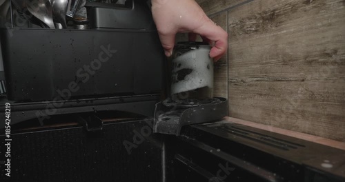 Unrecognizable woman's hand washing a soapy glass mug using a modern high-pressure rinser integrated into a kitchen countertop next to the sink, showcasing household chores and cleaning.