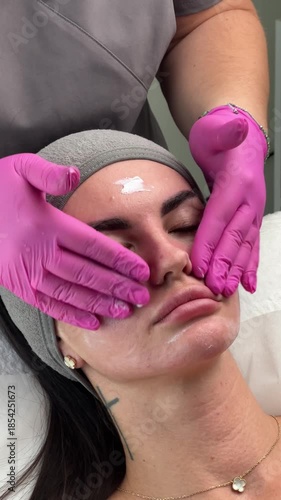 facial massage session. Aesthetician in pink gloves gently massages a woman face after cosmetic treatment. Close-up, professional skincare procedure.
