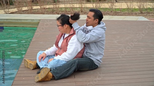 Couple sharing a tender moment as man ties woman’s hair ponytail in the park
