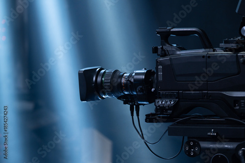 Professional broadcast camera capturing a live concert or event, recording the action with theatrical stage lighting creating dynamic light beams