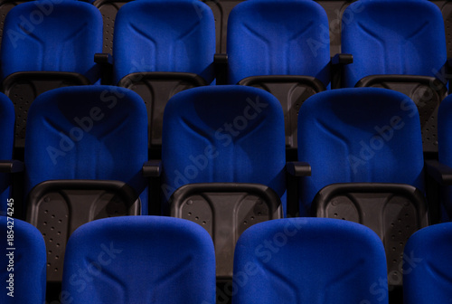 Rows of empty blue chairs providing seating in a modern auditorium, cinema, or conference hall with dark accents, implying an upcoming event or quiet space