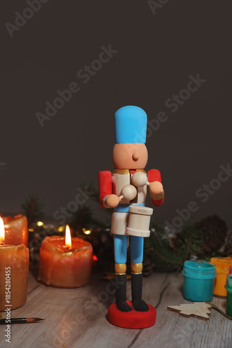 Wooden toy fairytale Nutcracker painted with colors, spruce branches, pinecones and candles on table on dark background