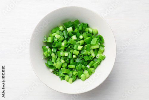 Cut fresh green onions in bowl on light wooden table, top view