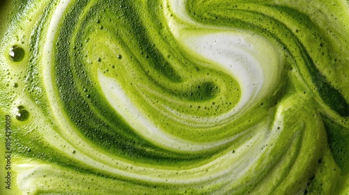 A close up view shows green liquid with white foam swirled in a cup. This drink is matcha made from powdered green tea blended with milk. The vibrant colors come from the matcha.