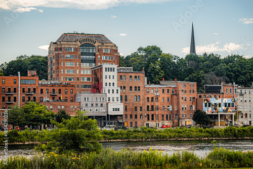 Looking across the Kennebec River to the town of Augusta, Maine surrounded by lush greenery on a summer evening