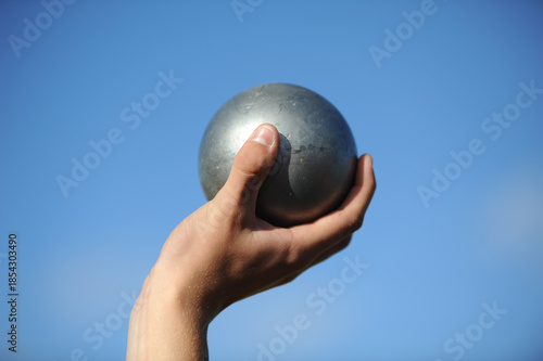 Hand holding metal shot put against clear sky.