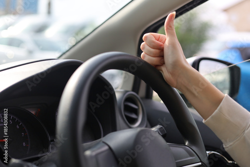 Positive Driving Gesture Inside Car. The hand shows the gesture super, cool, good, thumbs up on the steering wheel of the car.