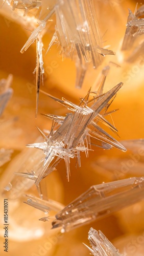 A close-up view of sharp, translucent, needle-like crystals against a warm, blurred background.