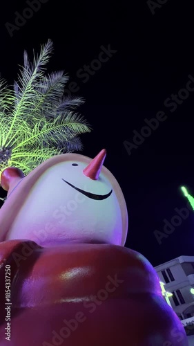 Illuminated snowman statue with palm tree background