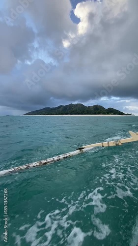 Vertical POV of a wooden boat sailing toward a tropical island. Essential inter-island transportation on turquoise water. Ideal for travel, adventure, and maritime lifestyle content.