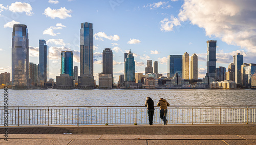 People overlooking Hudson River toward Jersey City skyline at golden hour