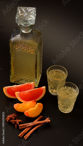 Homemade peach and grapefruit liqueur with cinnamon and anise on a black background in a crystal glass.