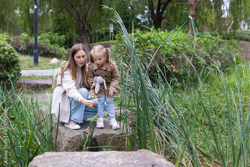 Canvas-taulu Mother and daughter exploring nature near a small stream in a park