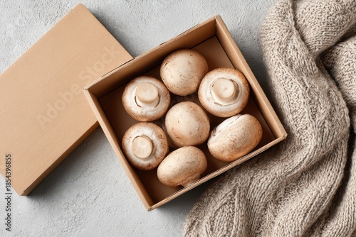 Fresh mushrooms in cardboard box with knitted blanket on grey background