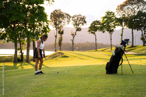 Hispanic woman golfer concentrating to strike ball on lush fairway at sunset, enjoying serene outdoor sport and summer leisure