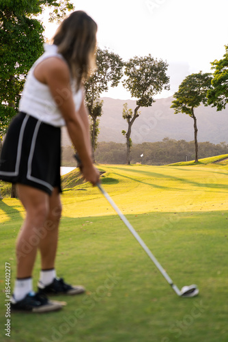 Hispanic woman golfer preparing for a golf swing on a green course during a beautiful sunset, enjoying an active luxury lifestyle