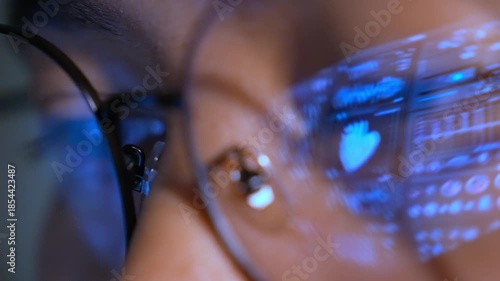 A person wearing glasses uses a laptop, with a real-time digital medical interface reflected in the lenses, representing healthcare analytics, clinical monitoring, and advanced medical technology.
