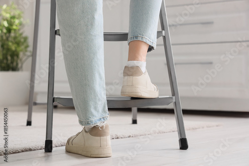 Photos Legs of woman getting on stepladder in room, back view