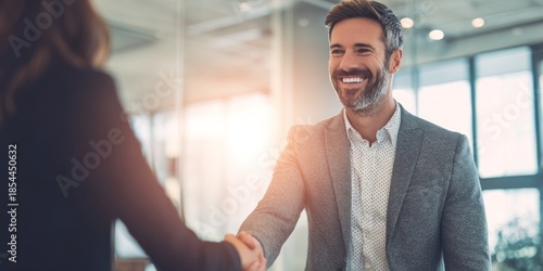 Wallpaper Mural A smiling man in a suit shakes hands with another person in a modern office setting, exuding professionalism and positivity. Torontodigital.ca
