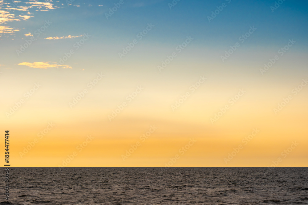 Obraz premium Nature sky breathtaking golden sunset over a calm ocean, with the entire sky and water bathed in brilliant shades of yellow and orange. Streaky clouds enhance the dramatic display of light 