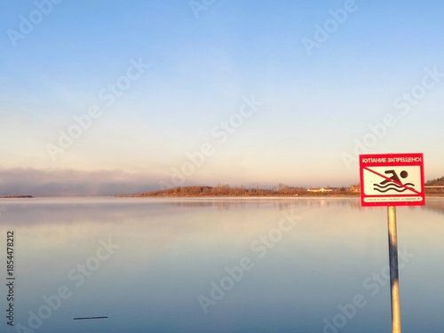 Calm lake with no swimming sign at sunrise: serene waterscape with clear sky