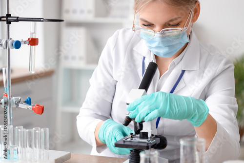 Female scientist with medical mask and microscope working in laboratory, closeup