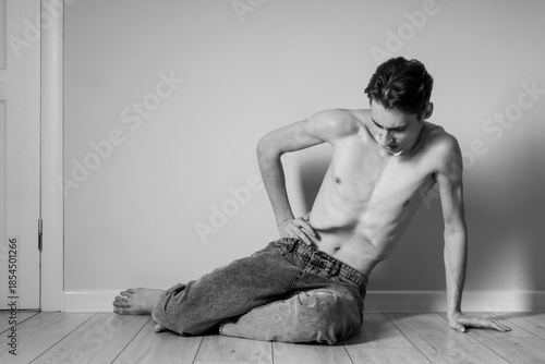 Tableau sur toile Young man with anorexia sitting near wall