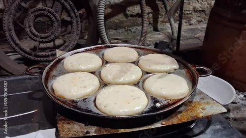Traditional Indonesian apem cake being cooked on a hot pan, showing the step-by-step street food baking process with soft batter rising into golden, fluffy cakes
