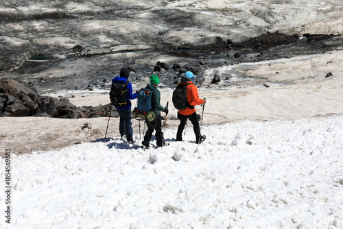 Two men and one woman are hiking on snowy and rocky terrain