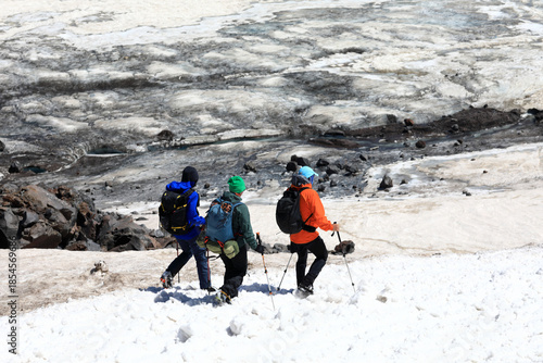 Three unrecognizable hikers ascending snowy mountain slope with trekking poles and backpacks