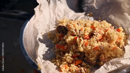Freshly cooked hot pilaf is placed on a parchment-lined tray outdoors. A delicious Kazakh ethnic dish. Close-up.