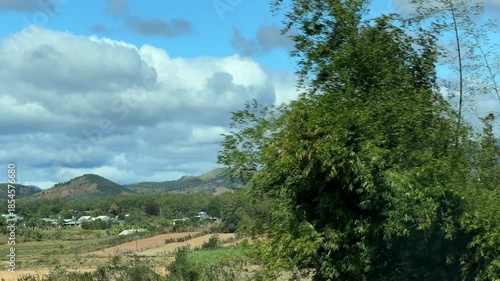 Plantations and open ground extend toward the horizon, softened by slow motion to suggest continuity between travel and land. Rural continuity.