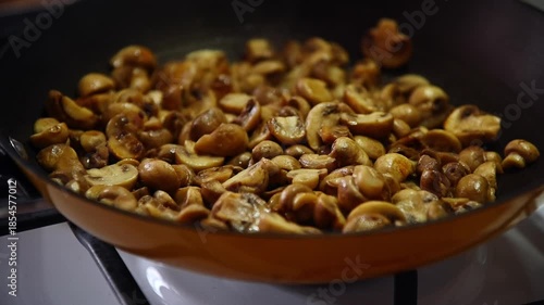 Close-up slow motion of small golden button mushrooms being fried in a pan on a home gas stove in the kitchen.
