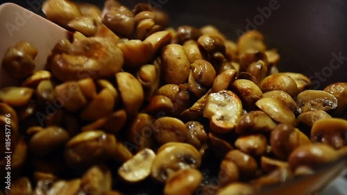 Close-up slow motion of small golden button mushrooms being fried in a pan on a home gas stove in the kitchen.