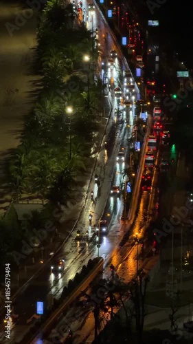 Traffic flows through a lit beachfront avenue while dark waves reach the shore, blending urban movement with the calm presence of the sea. Night seaside traffic, city coast.