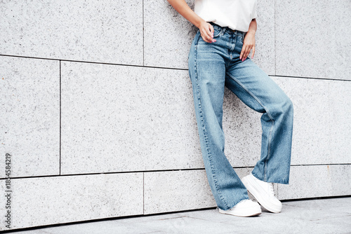 Young hipster woman in trendy summer white t-shirt and jeans clothes. Carefree woman, posing in the street at sunny day. Model outdoors near wall. No face