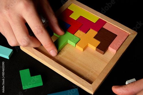 Close-up of hands solving wooden puzzle game on black background, logical thinking and mental health concept