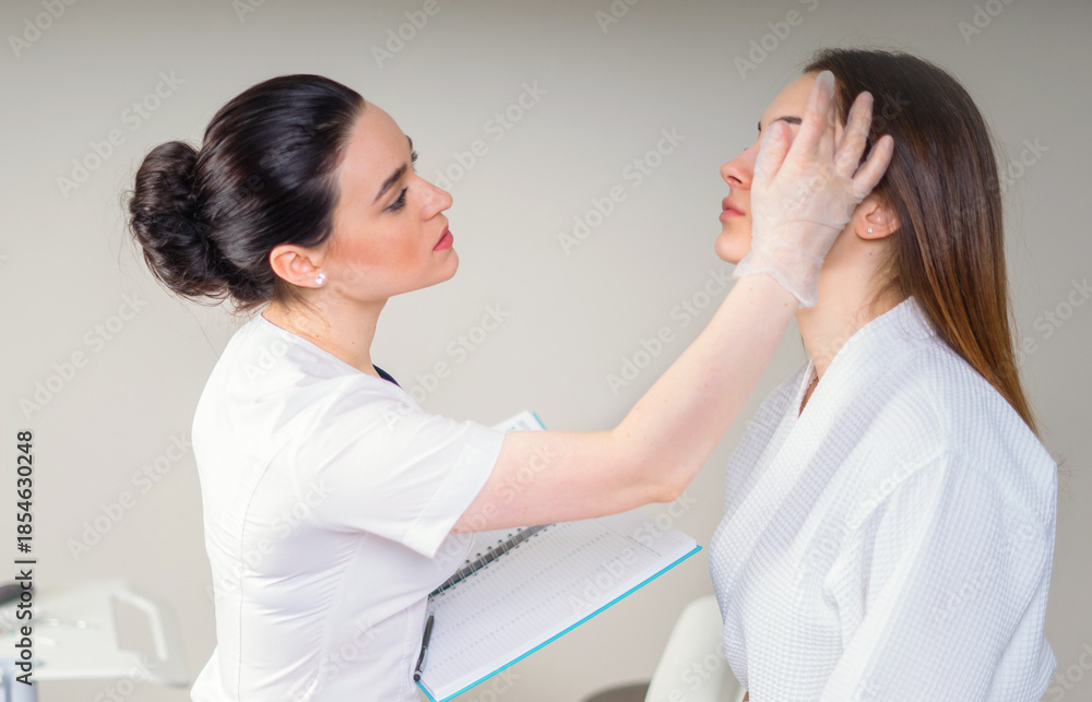 Obraz premium Professional cosmetician examining face skin of girl in clinic of esthetic cosmetology