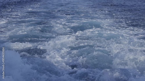 Churning ocean water creating white foam and turbulence from a moving vessel. Slow motion.